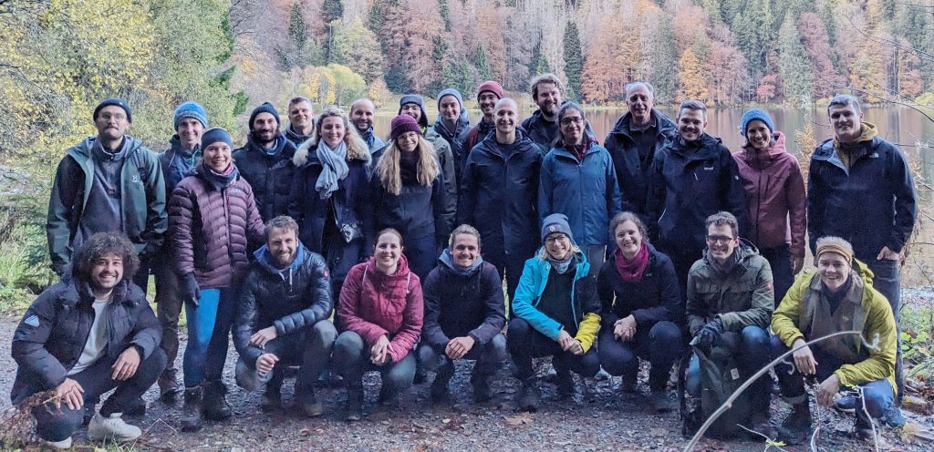 Picture of 26 people in hiking gear in front of an autumnal forest.